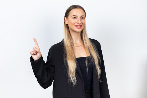 Female pointing up and looking at camer. Professional company business woman over white wall background