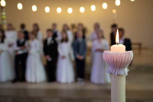 a lit candle with children in the background at first communion
