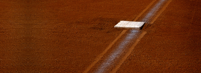 this photo is of a Baseball Player Running to third base on Baseball Field during Baseball Game. the third base is white. and infield of the baseball field is dirt with green grass in the outfield and foul line. the baseball player or athelete is running to third base during a live professional baseball game or little league baseball game. the lighting is natural sunlight during the afternoon or evening. this photo was taken at a live baseball game or sporting event. 
