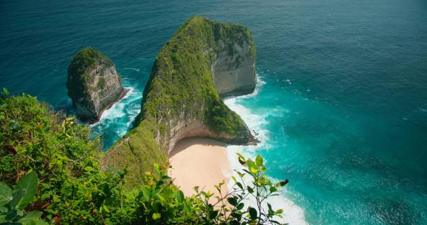 istock Blue ocean waves crashing on tropical rocky cliffs and sandy Kelingking beach. Top down view of turquoise sea water, green vegetation in Bali. 1490993678