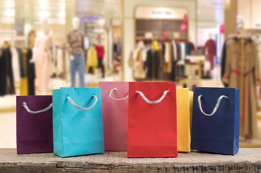 A lot of multi-colored paper shopping bags on a wooden table in a shop. Front view