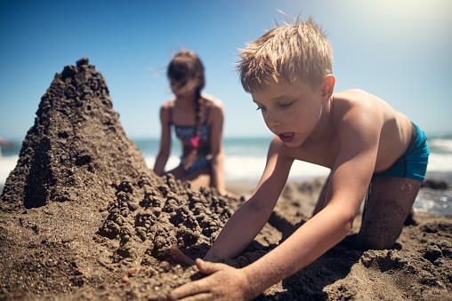 Two little kids having fun building a sandcastle on the beach. Brother and sister are aged 7 and 11.  
Sunny summer vacations day at sea. Costa del Sol, Andalusia, Spain.
Nikon D810