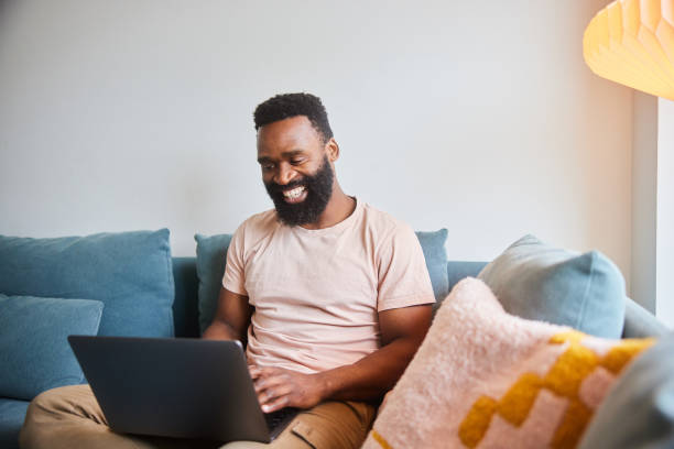 istock Man laughing and working on a laptop on his living room sofa 1491002124