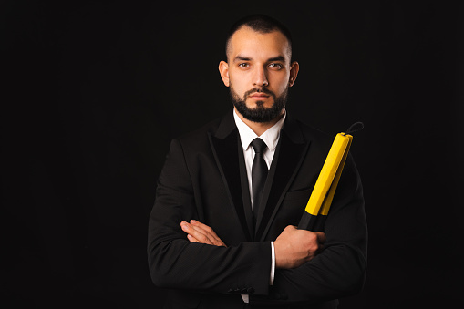 Front portrait of a strong serious man holding nunchaku and arms crossed. Studio shot over black background.