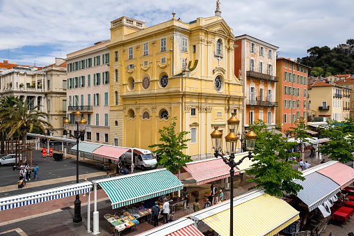 Nice, France - April 27, 2023: The famous market on Cours Saleya with visible striped roofs hiding the stalls from the sun. A large religious building is visible, this is The chapel of Mercy