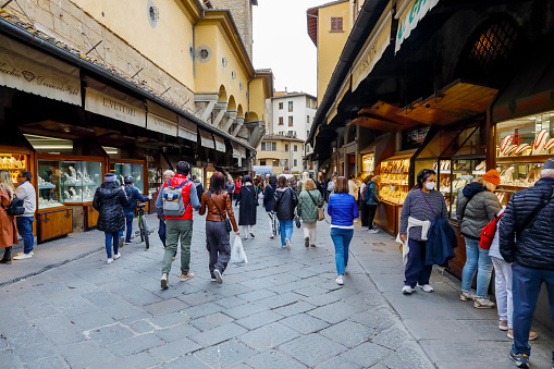 Florence, Italy - April 14, 2023: Tourists walking the famous medieval Ponte Vecchio (Old Bridge) which spans the Arno river. There are small shops on both sides along the bridge