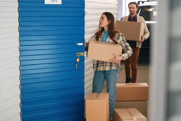 Photo of Young woman and man with big cardboard boxes into warehouse