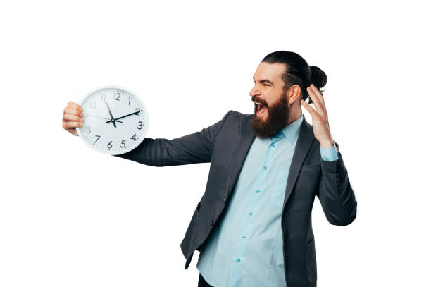 istock Shouting upset bearded man wearing jacket is holding a round white clock. 1491007296