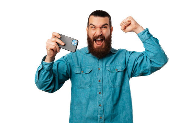 istock Ecstatic young bearded man is making the winner gesture while holding phone. 1491007709