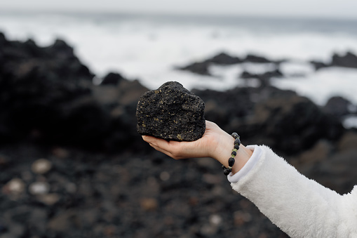 Close up of hand holding black volcanic basalt rock. Mosteiros beach - volcanic black sand beach in Sao Miguel, Azores.