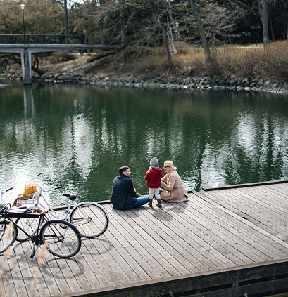 High angle view of father, mother and their daughter sitting by the river with their bicycles, talking and laughing.