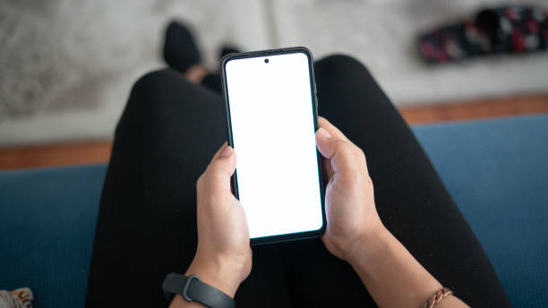 istock Woman using phone with white screen while sitting on sofa at home , mock up screen 1491020591