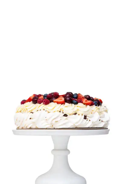 Meringue Pavlova cake with whipped cream and fresh berries isolated, strawberries and blueberries on white background. Vertical orientation