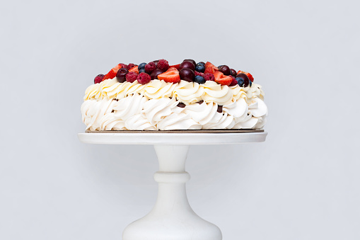 Meringue Pavlova cake with whipped cream and fresh berries isolated, strawberries and blueberries on grey background. Horizontal orientation