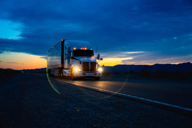 a white semi-truck drove through the nevada desert as the sun set behind the mountains. its silhouette stood out against the orange and pink sky, a lone traveler on the open road. - truck desert semi truck orange imagens e fotografias de stock