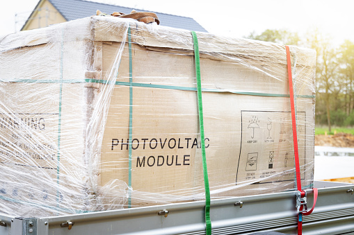 Photovoltaic modules packaged in a cardboard delivery box and strapped on a trailer.