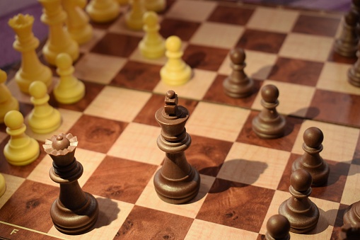 Leader and competition. White Chess King among lying down black pawns on chessboard, dark blue background.