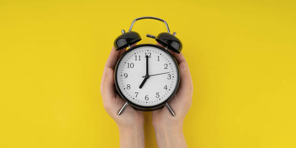 istock Woman's hands holding a black alarm clock on a yellow background 1491027055