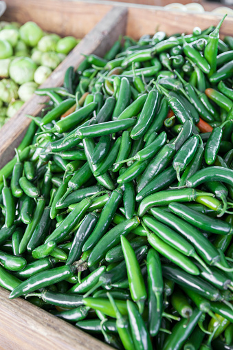 A heap of bright green chili peppers, with tomatillos in the background, on display at a farmer's market.