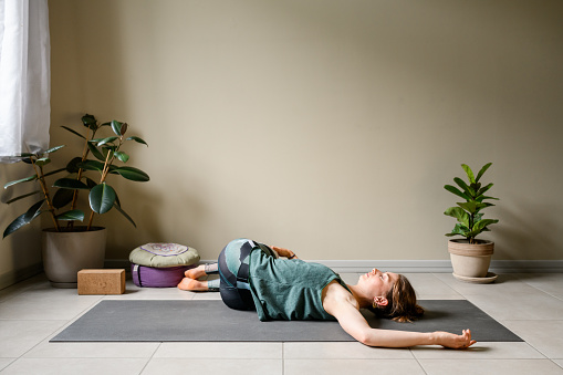 Professional woman practicing yoga at home: Supine Spinal Twist, Supta Matsyendrasana