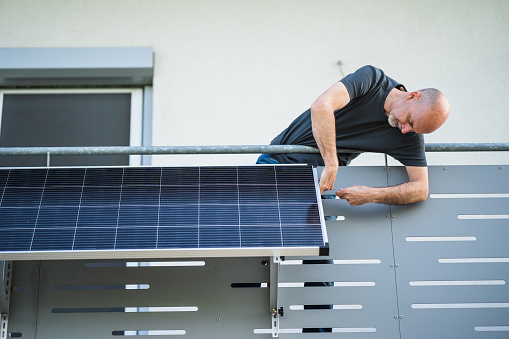 man installing adjustable solar panel on balcony of his house