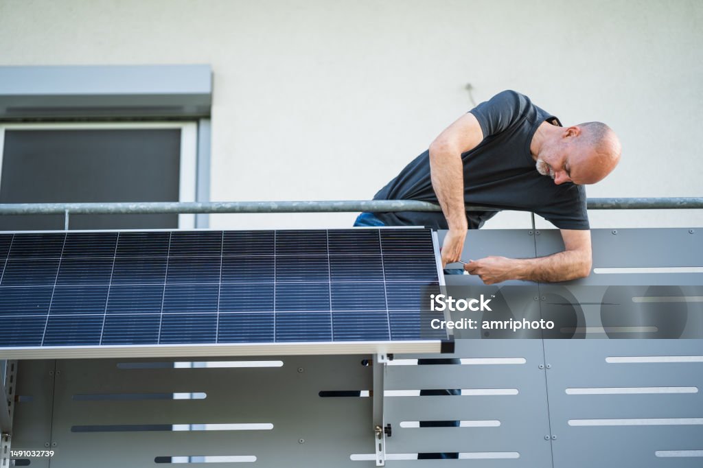 man mounting solar panel on balcony man installing adjustable solar panel on balcony of his house Solar Panel Stock Photo