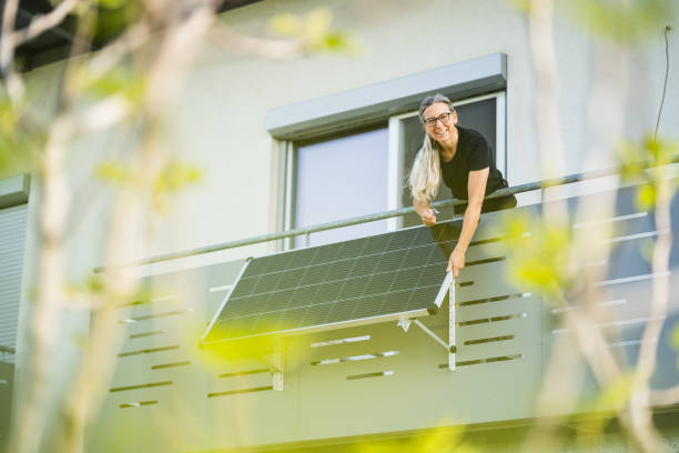 happy woman installing solar panel on houses balcony stock photo
