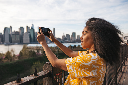 Woman take a snaps on mobile to New York skyline from Brooklyn streets in spring.