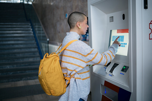 Young woman buying train ticket at the automatic vending machine on platform. Female commuter booking train ticket at railway station using vending machine.