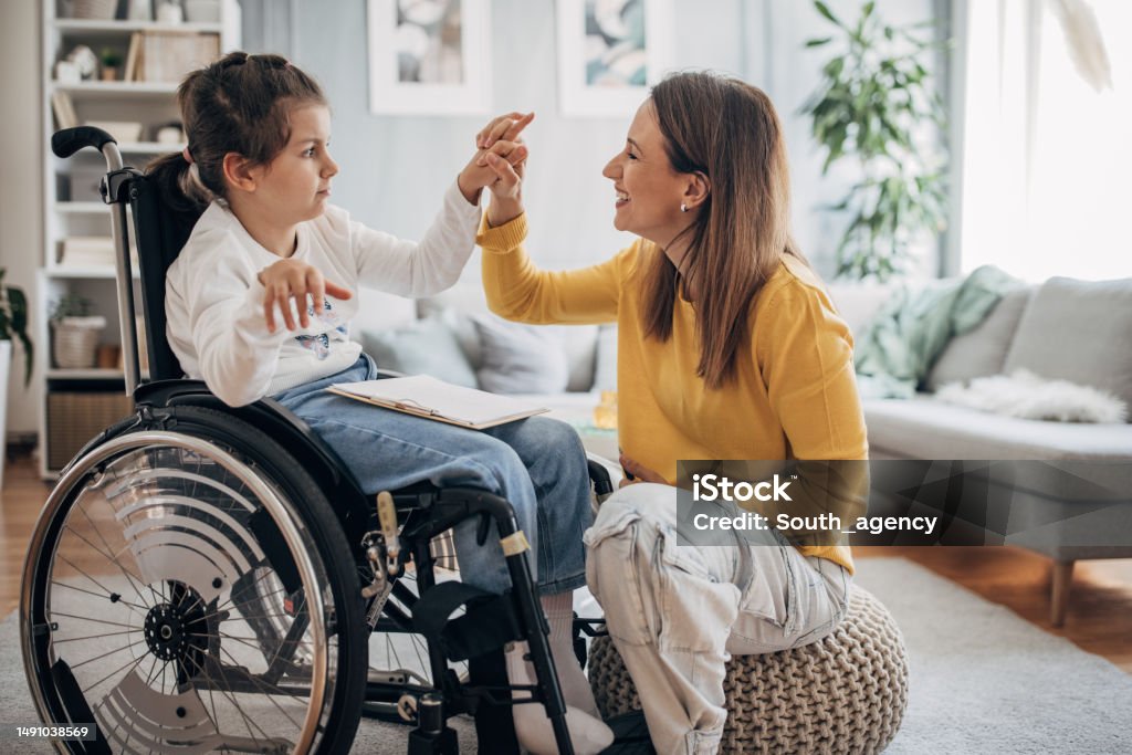 Mom and young daughter having fun Mother and young daughter who is in wheelchair enjoying together in living room at home. Disability Stock Photo