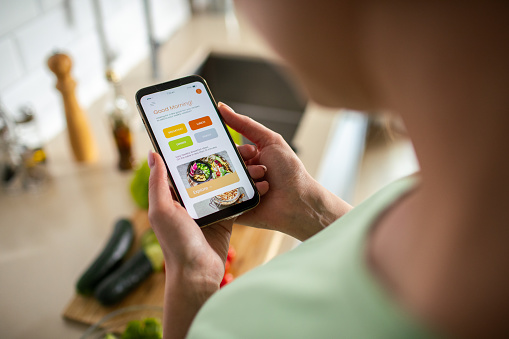 Close up of a Young woman using a diet app on her phone while preparing a healthy food dish at home