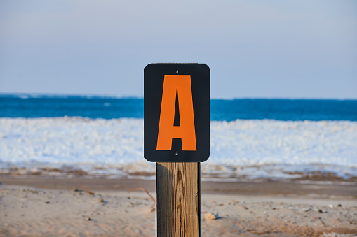 Signpost marker letter A on sandy beach with icy layer