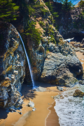 Image of Small waterfall pouring from coastal rocks onto a sandy ocean beach
