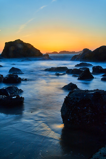 Image of Smooth waves around rocks on beach at golden hour in California