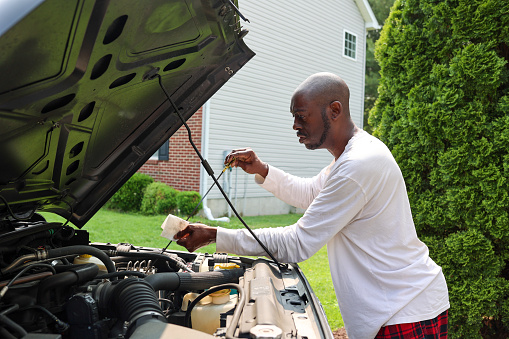 A portrait of a black man checking the oil level of a vehicle