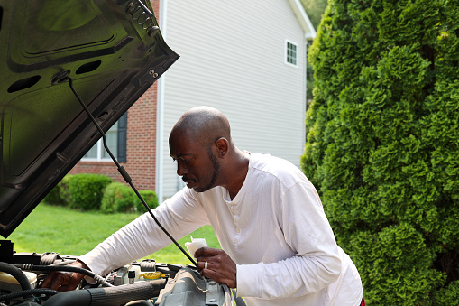 A portrait of a black man checking the oil level of a vehicle