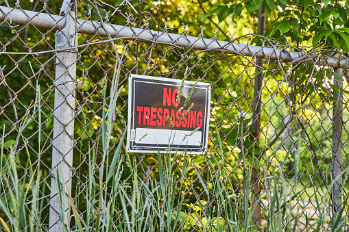 No trespassing sign in red text on metal fence in forest