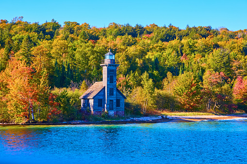 Image of Old wooden lighthouse on edge of island with forest behind it and calm lake ocean or sea water in front of it