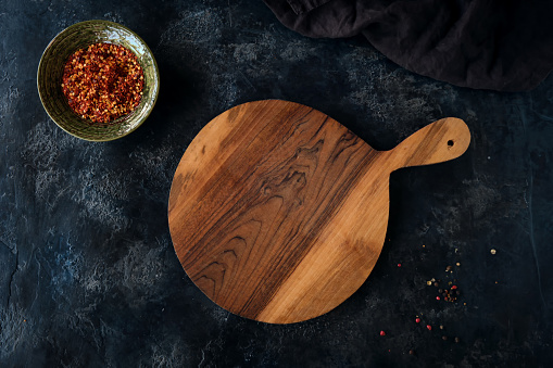 Top view of a beautiful empty cutting board, a bowl of red spices, and a decorative cloth on a dark blue background. Template for Mockup.