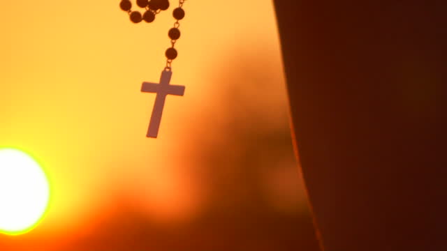 Praying with cross on beautiful sunset
