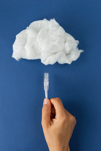 Hand is holding ethernet cable under white cloud on blue background. Representing internet connection and cloud technology.