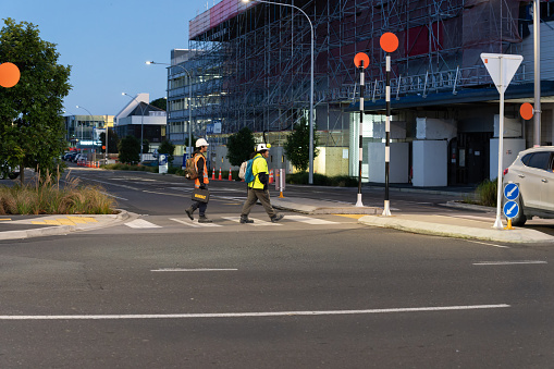 Tauranga New Zealand - May 17 2023; Workers in hi-vis vests crossing street on way to construction site in city.
