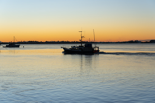 Commercial fishing boat leaving Tauranga in morning light in silhouette