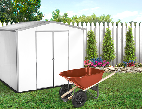 White shed in a backyard with green grass and a wheelbarrow