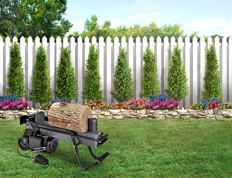 Log splitter in a backyard with green grass and wood fence