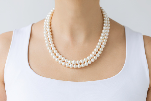 Chest of unrecognizable female is wearing  white pearl necklaces in front white background.
