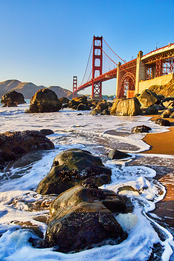 Image of Waves crash around rocks on beach next to Golden Gate Bridge in San Francisco near sunset