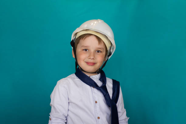istock A handsome boy smiling cutely at the camera in a white construction helmet and shirt on a blue background. Child builder isolated in a construction helmet. The concept of the future of the child. 1491055556