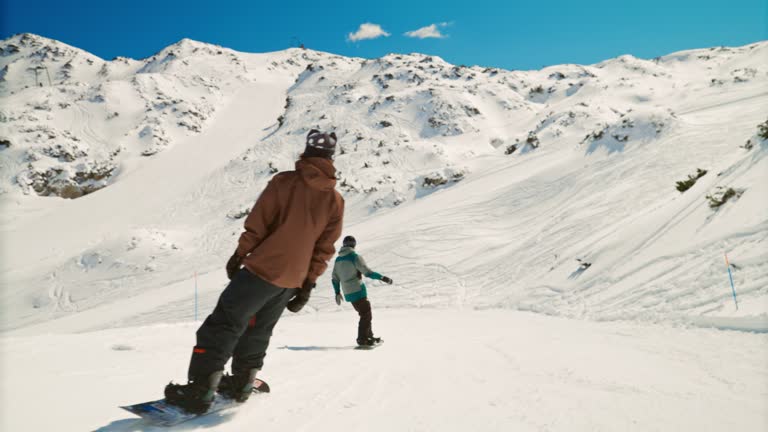 SLOW MOTION shot of male friends snowboarding on mountain. Men are enjoying winter sport. They are on snow during sunny day.