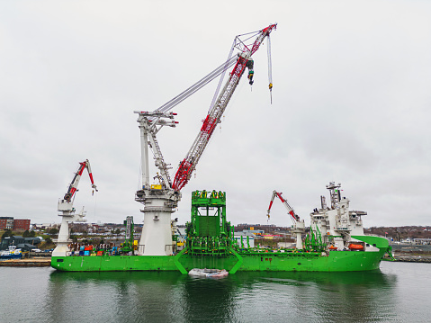 A water level view of a heavy lift vessel used in offshore wind farm construction docked on an overcast afternoon.